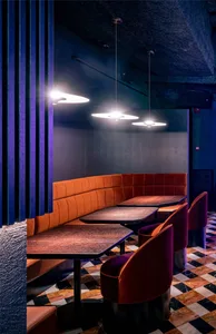 A stylish restaurant interior with velvet booth seating, wooden tables, and marble flooring.