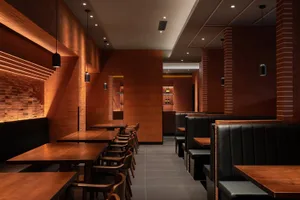 Modern industrial restaurant interior featuring wood tables, black leather seating, and brick walls.