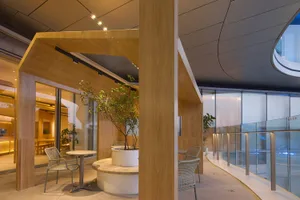 Modern coffee shop terrace with wooden pergola and glass walls, featuring a potted plant and seating area.