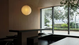 Minimalist modern restaurant interior with large windows, wooden seating and tables, and a lantern light hanging overhead.