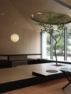 A modern restaurant interior with minimalist design featuring wooden elements and a tree in the center.