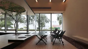 Modern restaurant interior with a wooden floor, tables, and chairs, featuring large windows with trees and greenery visible o