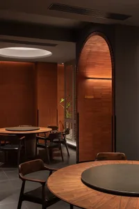 Modern restaurant interior with round wooden tables and metal chairs.