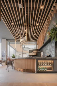 Modern cafe bar interior with wooden slat ceiling, marble countertop, and glass bottles.