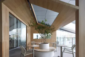 A modern cafe interior with wooden walls and tables, featuring a large potted plant in the center.
