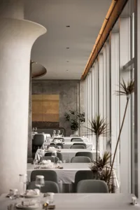 A minimalist restaurant interior with white walls, concrete columns, and large windows.