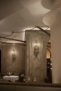 A modern restaurant with a concrete floor and stone walls, featuring elegant sconce lighting.