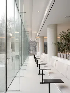 Modern restaurant interior featuring white marble tables and black chairs surrounded by large glass walls.