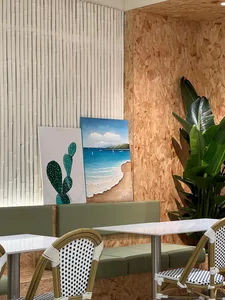 A cafe bar with green benches, white tables, and wall art featuring a beach and plants.