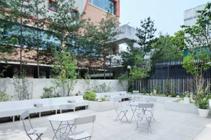 Concrete outdoor seating area with white furniture, greenery, and garden tiles.