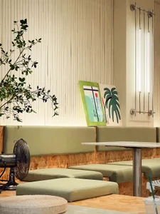 A modern cafe interior featuring a green sofa, white tables, and hanging lights.