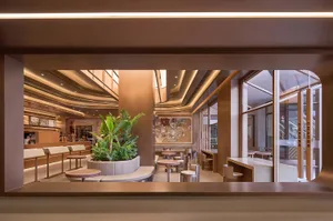 Interior view of a modern coffee shop featuring concrete and glass elements, with seating and plants.