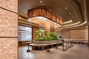 A modern coffee shop with neutral-toned interior design featuring cozy seating, greenery, and a warm lighting setup.