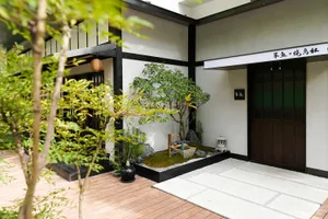 A serene minimalist entrance yard with wooden walkway, grass, and stone elements.