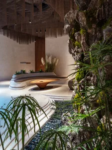 Modern spa relaxation room with natural stone and concrete surfaces, wood accents, and a flowing water feature.