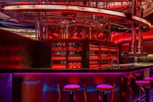 A modern industrial bar interior with metal and glass elements illuminated by neon lighting.