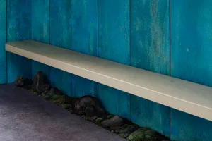 A minimalist floating shelf mounted on a blue wall with a textured surface.