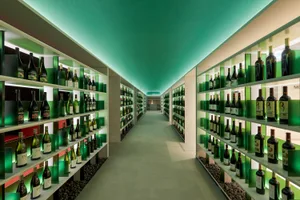A minimalist wine tasting room with glass walls and shelves filled with wine bottles.
