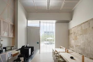 Modern minimalist cafe interior featuring wooden tables and chairs, glass dividers, and white walls and ceiling.
