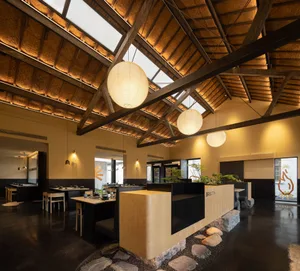 A minimalist restaurant interior with a high ceiling, recessed lighting, and wooden materials.