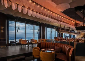 A modern bar restaurant with a leather seating area, ceiling lights, and a view of the water.