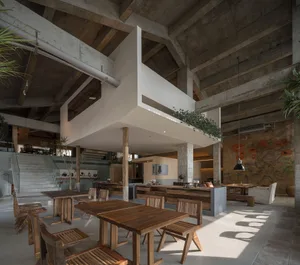 Industrial-style cafe interior featuring wooden tables, concrete ceiling, and exposed beams.