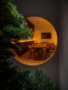 A minimalist conference room featuring a long wooden table and chairs, with a round entryway and warm lighting.