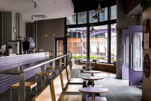 An image depicting the interior of a modern coffee shop with wooden seating, metallic hanging lights, and concrete walls.