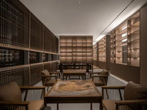 A modern study room with wooden tables and chairs, featuring a large central table with a stone surface and bookshelves on th