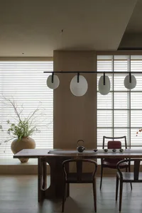 A modern dining room features a wooden table with a minimalist design, surrounded by chairs and topped with a tea kettle and