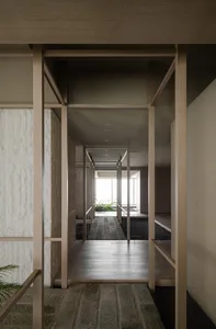 A modern interior corridor with wooden walls, floors, and railings, leading to a well-lit space with a view of greenery.