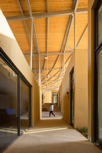 A minimalist campus hallway with concrete walls, steel beams, and wooden ceiling beams.