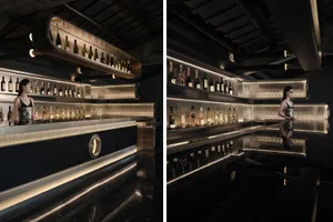 Modern bar with glass shelves displaying various bottles of alcohol and modern interior design elements.