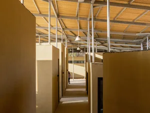 A minimalist interior space with concrete walls and a wooden ceiling, featuring a walkway with a person walking.