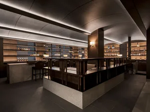 Industrial design bar counter with metal railings, wooden seating, and stone base.