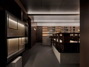 A modern restaurant bar with wooden interiors and shelves filled with bottles.