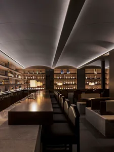 A modern restaurant bar with wooden counters and shelves filled with bottles.