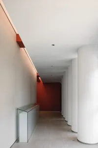 A minimalist corridor with glass cylinders and red accents on a white wall.