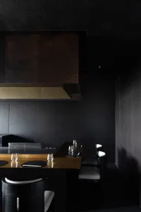 A minimalist design featuring black leather chairs, black metal table, and a black wall with a golden counter.