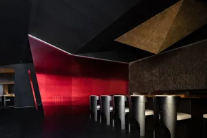 A sleek, modern restaurant interior featuring a glass bar counter with a geometric ceiling design.