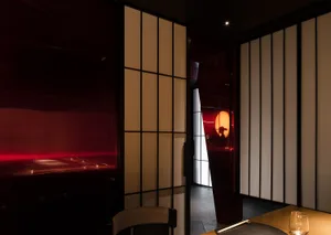 Modern restaurant interior with wooden curtains, red light, and sleek furniture.