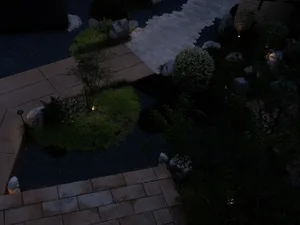 A nighttime view of a garden pathway with stone and gravel materials and illuminated plant beds.