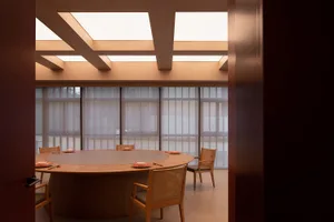 A modern dining room with a circular table, wooden chairs, and skylights letting in natural light.