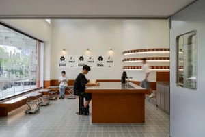 A modern coffee shop interior with a wooden bar counter and seating area, featuring a minimalist design with white walls and 