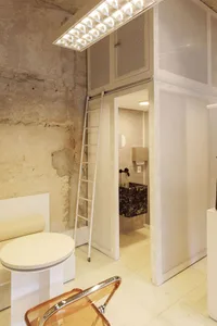 A modern office space with concrete walls, a stone table, and a ladder leading up to a loft area.