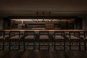 A dark, industrial-style restaurant kitchen with metallic elements and a long bar.