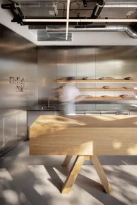 A minimalist restaurant interior with a wooden counter and stainless steel background.