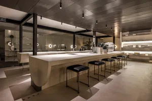 A modern coffee shop with a minimalist aesthetic, featuring a concrete bar counter, black stools, and white walls with floor-