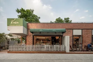A modern restaurant exterior featuring a brick wall and a green awning with the name 'Kaka' on it.