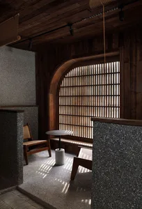 Modern coffee shop interior with concrete and wood materials, featuring a small table and chair under an arched, shuttered wi
